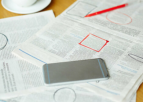 Jobsuche: Zeitungsanzeigen und Smartphone liegen ausgebreitet auf einem Tisch