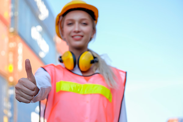 Arbeitgeberattraktivität: Frau mit Helm und Warnweste zeigt mit dem Dauem nach oben