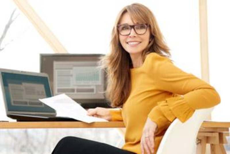 Eine Frau im orangenen Pullover sitzt am Schreibtisch
