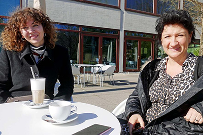 Mentee Lucija Misetic (links) sitzt mit Mentorin Romana Augenstein (rechts) vor einem Café am Tisch
