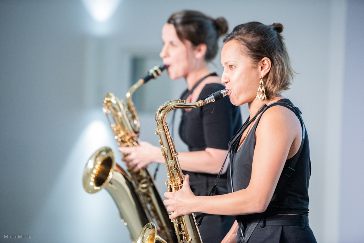 Zwei schwarz gekleidete Frauen stehen nebeneinander und spielen Saxophon.